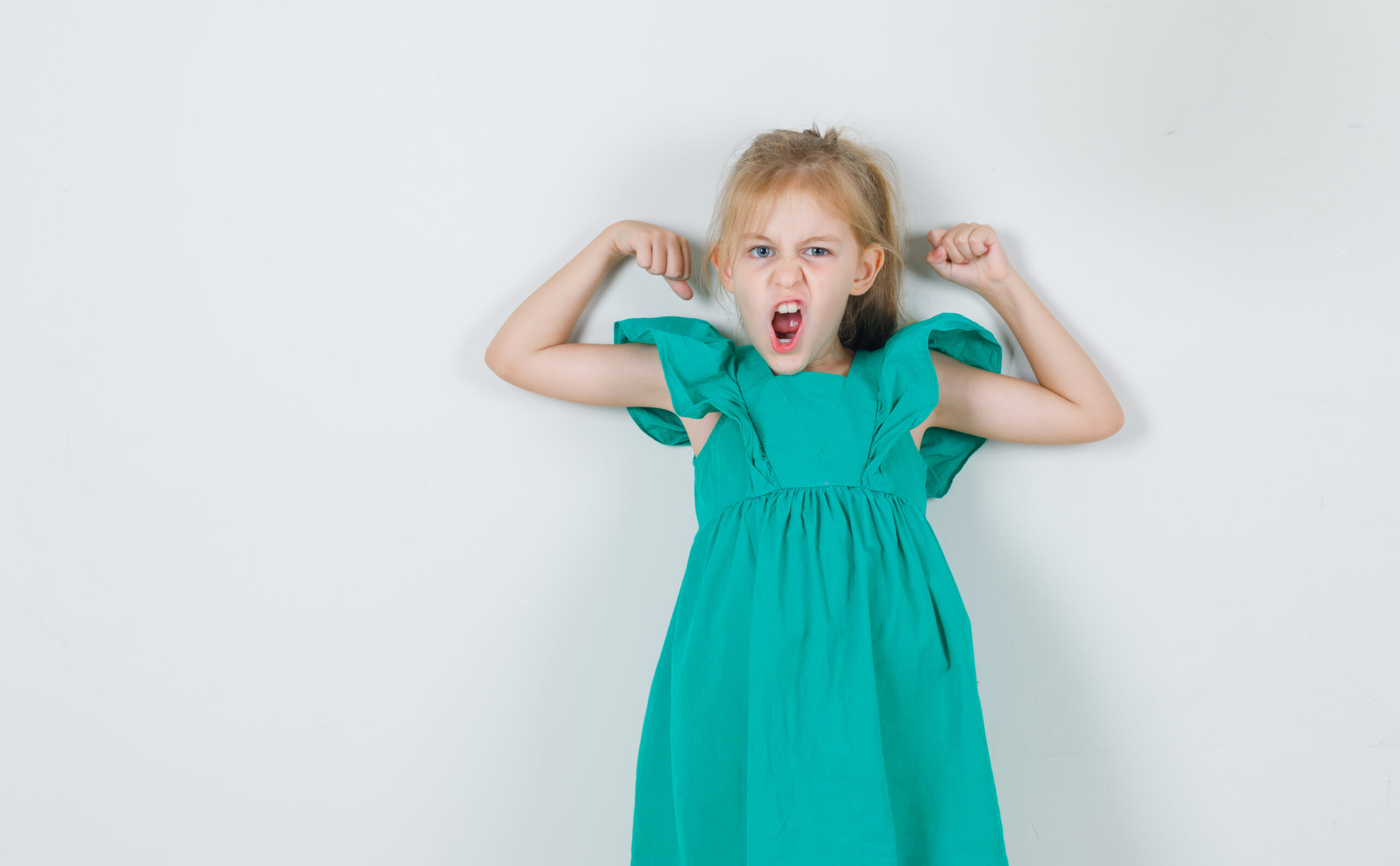 Little girl in green dress showing muscles angrily , front view.