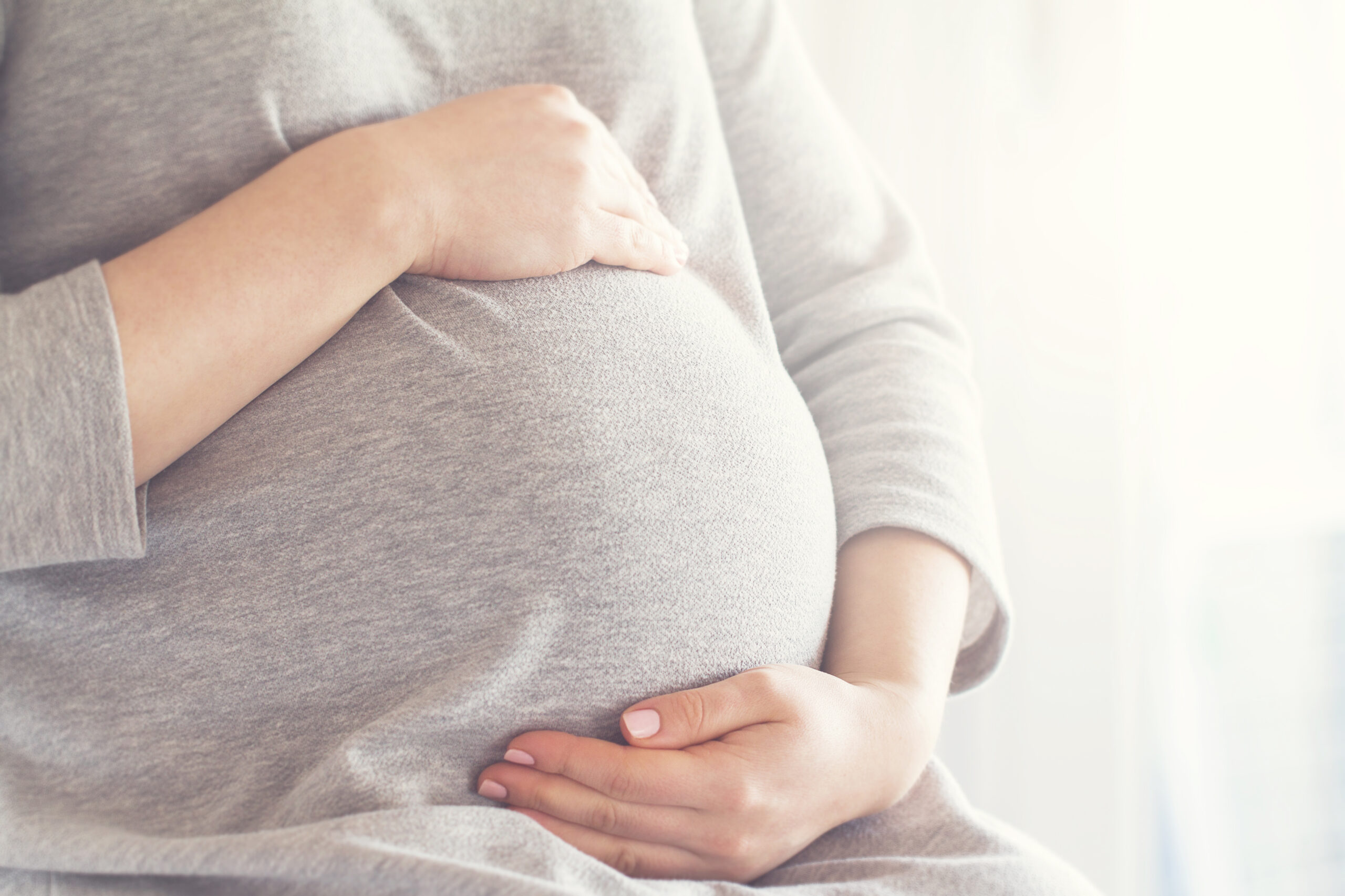 Young pregnant woman holds her hands on her swollen belly. Love